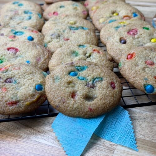 M&M'S cookies on a wire rack, with a blue ribbon sitting on top of a wooden table .