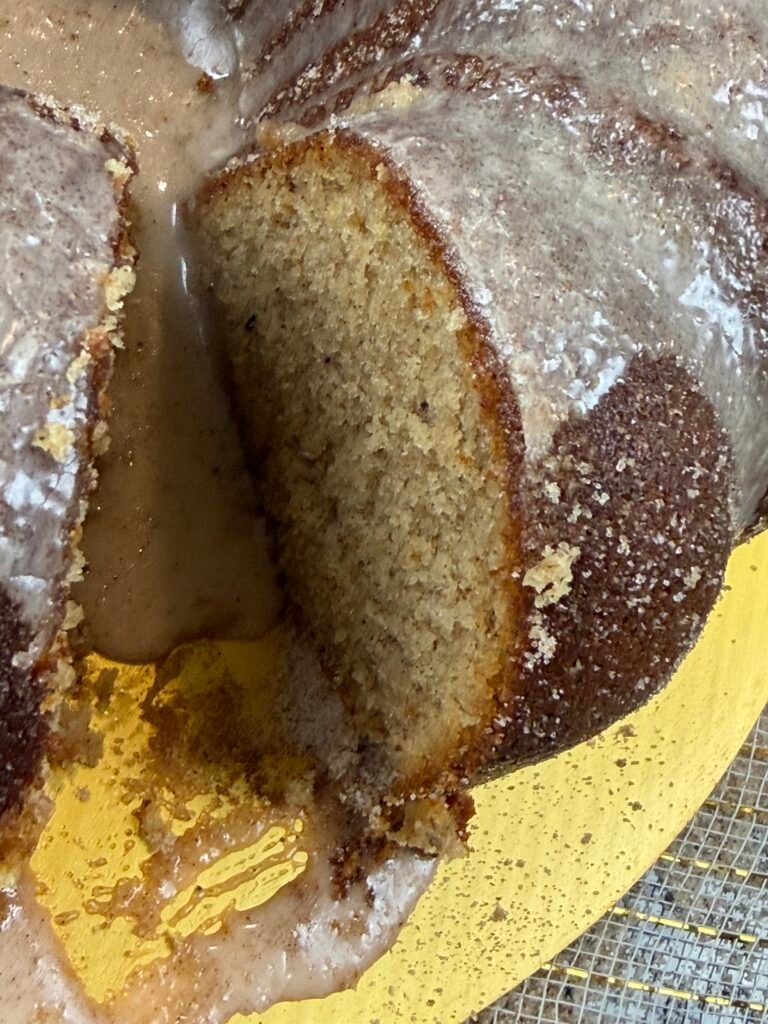 An Apple Cider Bundt Cake on a golden plate with a piece cut and sits to the side.